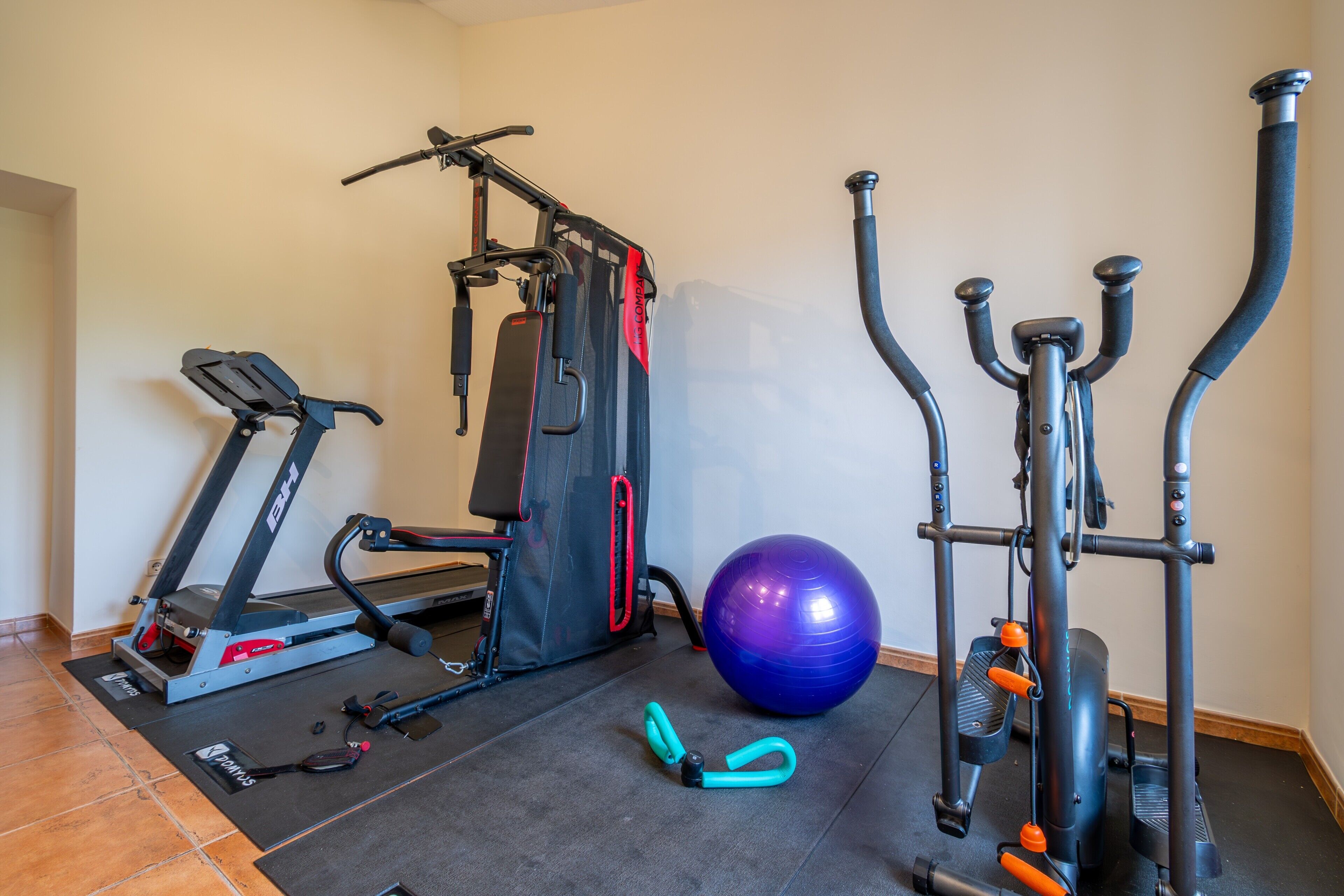 A home gym with a treadmill, weight machine, elliptical, and exercise ball.