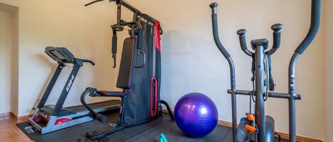 A home gym with a treadmill, weight machine, elliptical, and exercise ball.