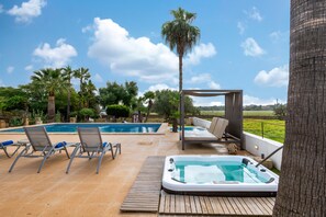 Uma área de piscina com espreguiçadeiras, hidromassagem e um pérgola.