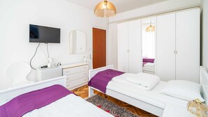 A modern bedroom with a television, a wardrobe, and a bed with a purple blanket. - 3 bedroom apartment with balcony (Mokosica)