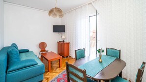 A modern living room with a sofa, a dining table, chairs, a TV, and a cabinet. - 3 bedroom apartment with balcony (Mokosica)