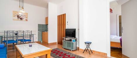 Una sala de estar moderna con un sofá, una mesa de comedor, un televisor y una zona de cocina.
