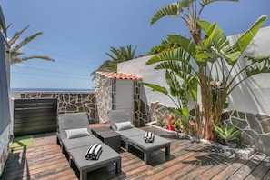 Un patio con mobiliario exterior, un muro de piedra y plantas tropicales.