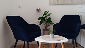 A room with two dark blue chairs around a small white table with a woven placemat. There is a potted plant on the table.