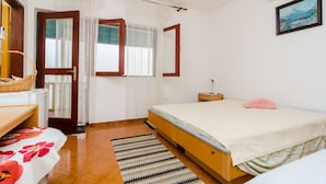 A bedroom with a bed, a bedside table, a nightstand, a window with curtains, a wall-mounted air conditioner, and a framed picture.