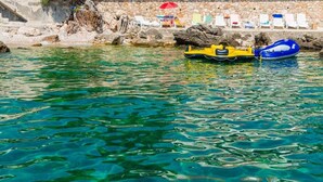 Una piscina azul cristalina con botes inflables, un muro de piedra y sillas de descanso.