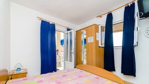 Un dormitorio con cama, mesita de noche, armario de madera, ventana con cortinas y un reloj de pared.