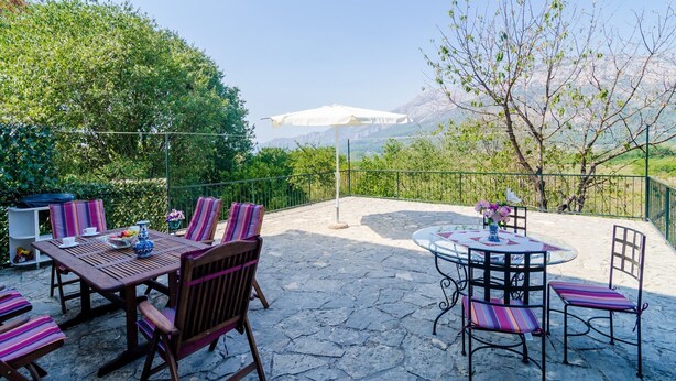 An outdoor patio with a stone floor, wooden and metal furniture, and a view of mountains.
