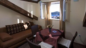 Ein gemütliches Zimmer mit einer braunen Couch, einem Esstisch mit roter Tischdecke und Blick auf eine Berglandschaft durch ein Fenster.