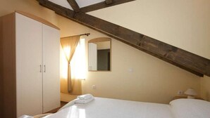 Ein Schlafzimmer mit einem großen Bett, einem Kleiderschrank, einem Spiegel und einem Fenster mit Vorhängen.