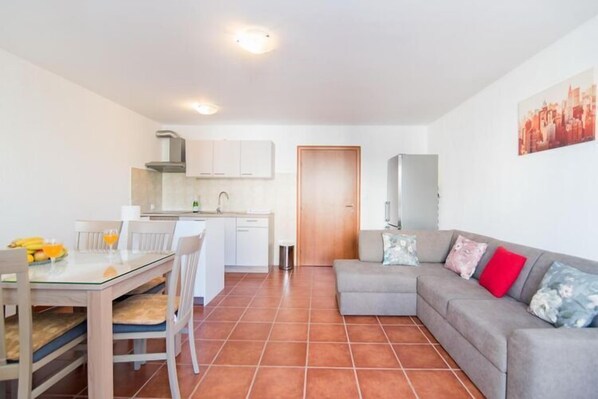 A modern apartment with a dining area, kitchenette, and a living room with a sofa and a TV.
