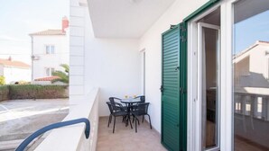 A balcony with a table and chairs, a sliding glass door, and a view of the street.