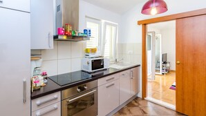 Une cuisine moderne avec des meubles blancs, un four à micro-ondes et une porte en bois donnant sur un espace de vie.