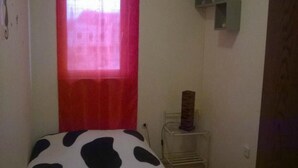 A small room with a bed, a window with a red curtain, a small shelf, and a bedside table with a vase. - Apartment Roksy - Two-Bedroom Apartment with Terrace and Sea View (ST) (Supetar)