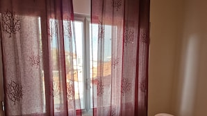 A dining area with a glass table and white chairs, a window with red curtains, and a tiled floor. - Polvere di Stelle (Altamura)