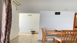 Un coin repas avec une table et des chaises en bois, une petite poubelle et un climatiseur fixé au mur.