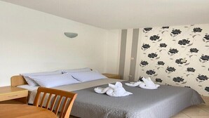 Une chambre d’hôtel avec un lit, une chaise en bois, une petite table et un mur orné d’un motif floral.