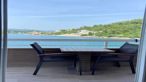 Un balcon avec une table et deux chaises, donnant sur une plage et un paysage vallonné.