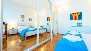Un dormitorio moderno con un espejo grande, una cama con ropa de cama azul, una mesita de noche y una repisa con botellas.