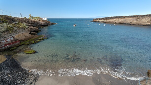 A coastal scene with a boat, clear water, rocky shore, and a building on the left.