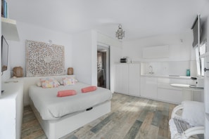 Une chambre moderne avec un grand lit, une armoire blanche, une salle de bain avec un lavabo et un miroir, et un élément décoratif mural.
