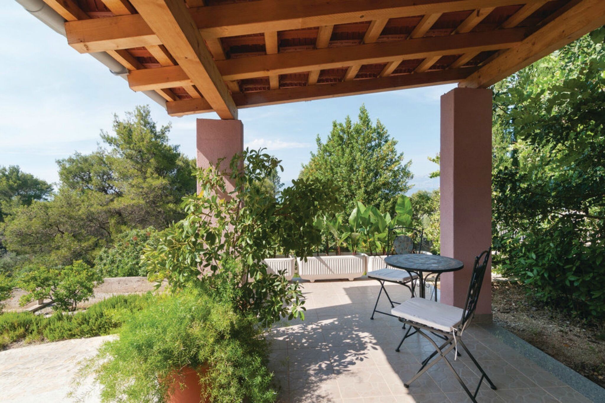 Un patio coperto con tavolo e sedie, immerso nel verde e alberi.