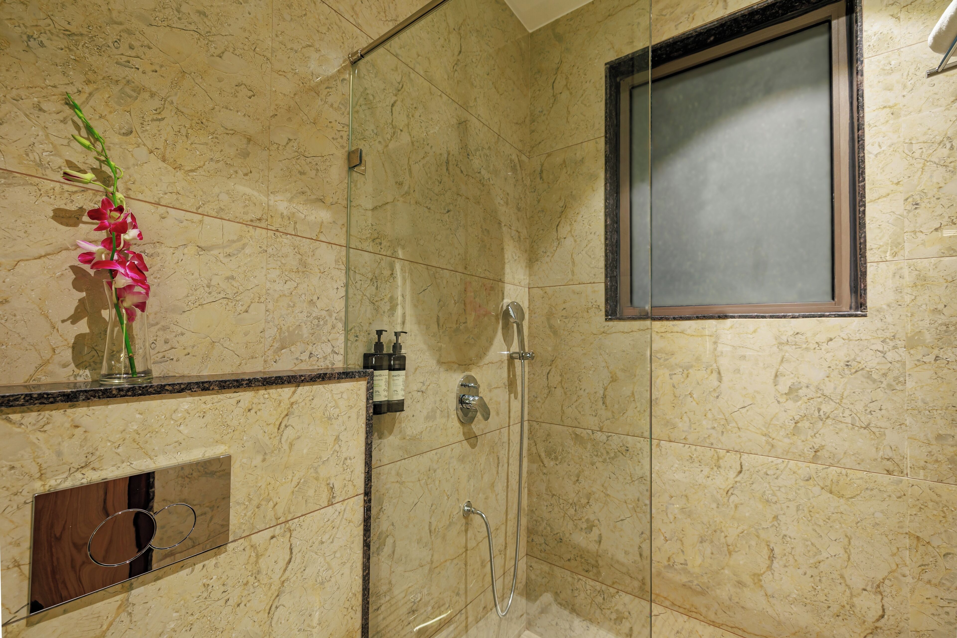A modern bathroom with a glass shower enclosure, marble tiles, and a small mirror.