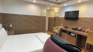 Een hotelkamer met een bed, een bureau, een stoel, een televisie en een plafondventilator.