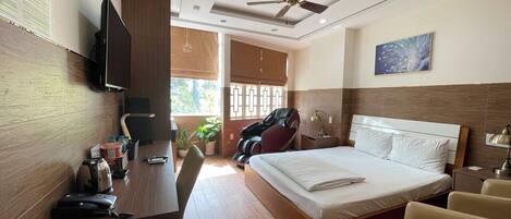 A hotel room with a bed, desk, chair, massage chair, and a ceiling fan.