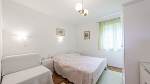 Ein Schlafzimmer mit einem Bett, einem Nachttisch, einer Kommode und einem Fenster mit Vorhängen.