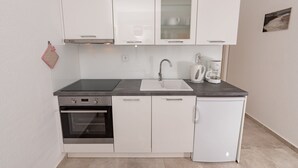 Eine kleine Küche mit weißen Schränken, einem Backofen, einer Spüle und einer Kaffeemaschine.