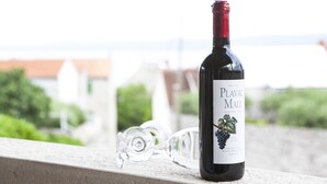 Eine Flasche Plavac Mali Wein mit einem Glas auf einem Balkongeländer.