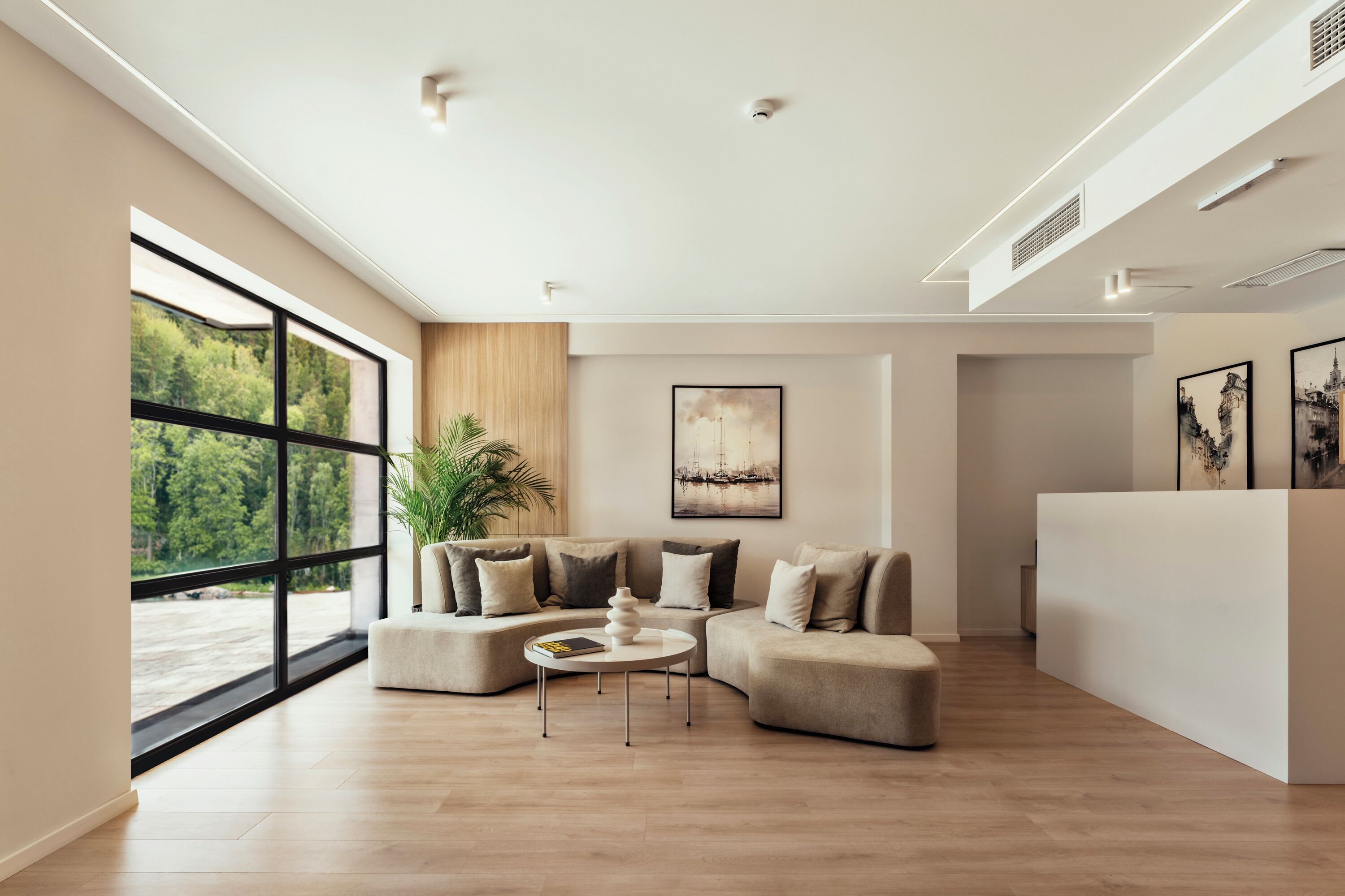A modern living room with a large window, a sectional sofa, a coffee table, and a white reception desk.