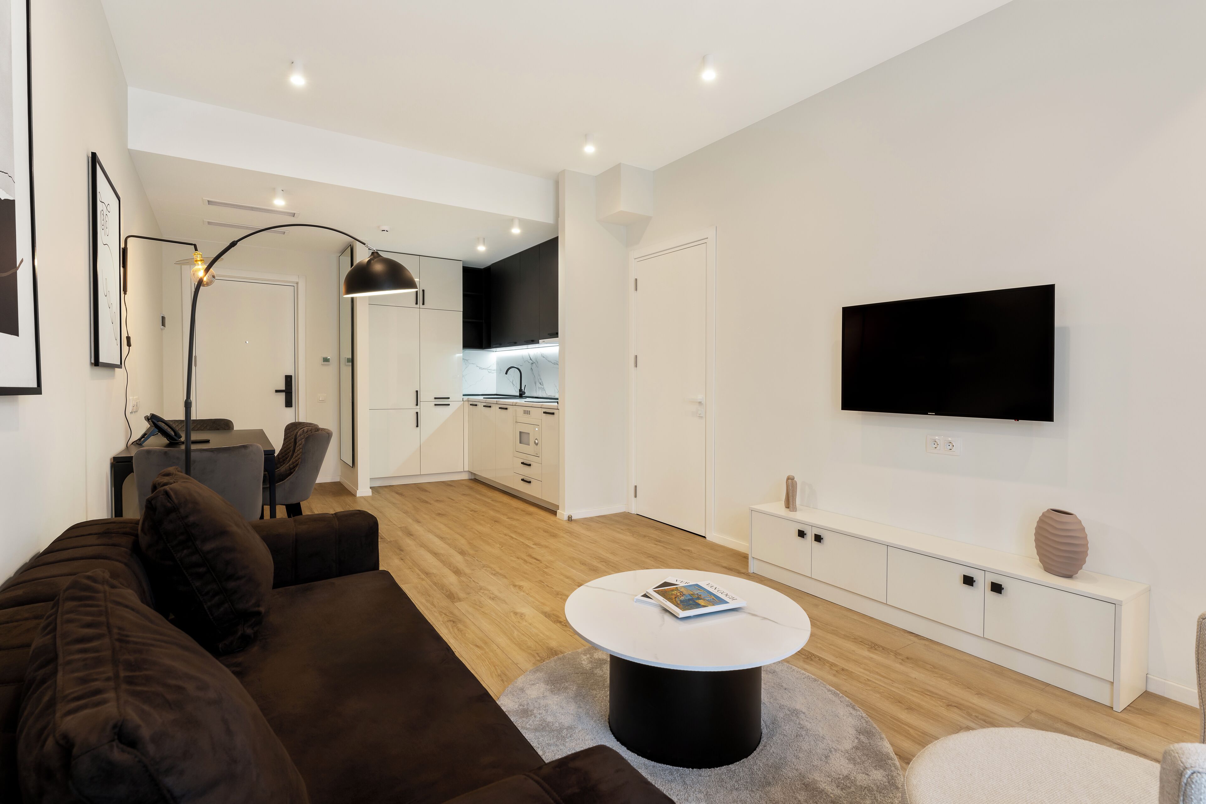 A modern living room with a brown sofa, a round coffee table, and a flat-screen TV mounted on the wall.