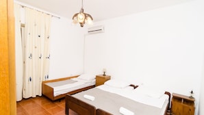 Ein Zimmer mit zwei Holzbett, einem Nachttisch, einem kleinen Tisch, einer Pendelleuchte und einem Vorhang.