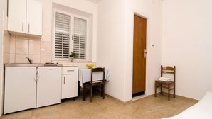 A compact kitchen with white cabinets, a small table, and a wooden chair. - Guest House Kiko - Apartment with Balcony (A5) (Pomena)