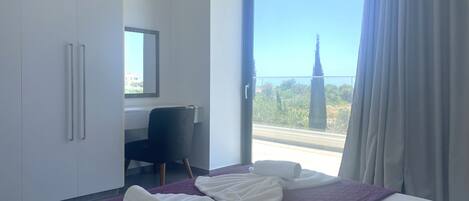 A hotel room with a bed, a desk, and a view of a building through the window.