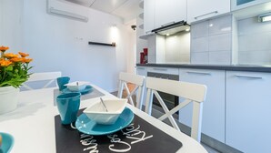 A modern kitchen with white cabinets, a black countertop, and a dining area with a white table set with blue dishes and a potted plant. - Apartment Simović - Two Bedroom Apartment with City View (Dubrovnik)