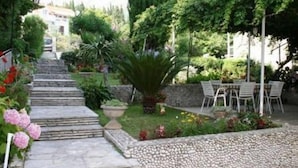 Un jardín con escalones de piedra que conducen a un espacio de descanso con sillas y una mesa.