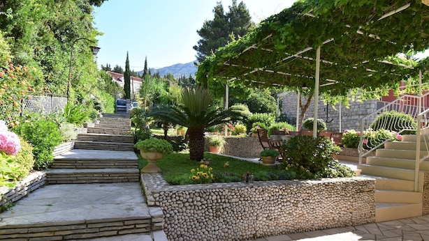 Una escalera de piedra conduce a un jardín con un pérgola, rodeado de plantas y un muro de piedra.