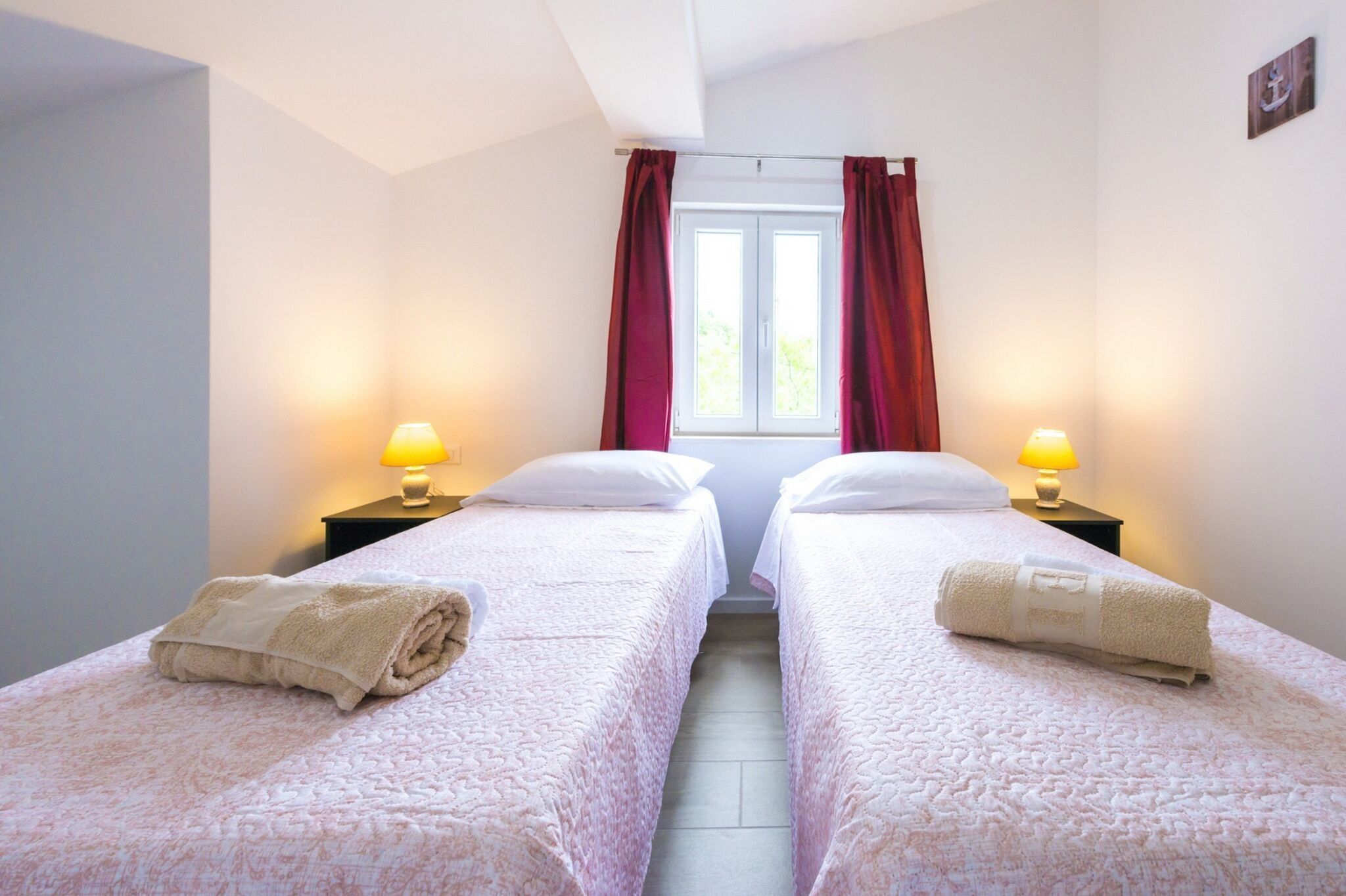 Een hotelkamer met twee eenpersoonsbedden, elk voorzien van een kussen en een opgerolde handdoek. Aan weerszijden van de bedden staan nachtlampjes.