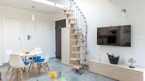 Un salon moderne doté d’un escalier en colimaçon, d’un coin repas avec des chaises bleues, d’une table en verre et d’un téléviseur à écran plat fixé au mur.