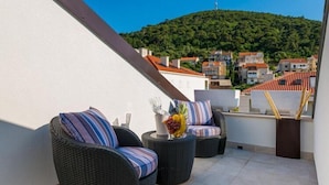 Un balcon agrémenté de meubles en osier, un vase rempli de fleurs et une vue sur une colline parsemée de bâtiments.