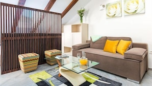 Un salon moderne avec un canapé marron, des poufs colorés, une table basse en verre et des œuvres d’art abstraites accrochées au mur.