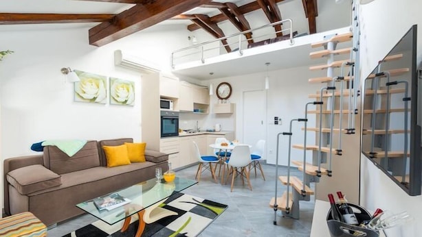 Un salon moderne avec une table basse en verre, un canapé et un coin repas comprenant des chaises et une table. Un escalier avec une rampe mène à un niveau supérieur.