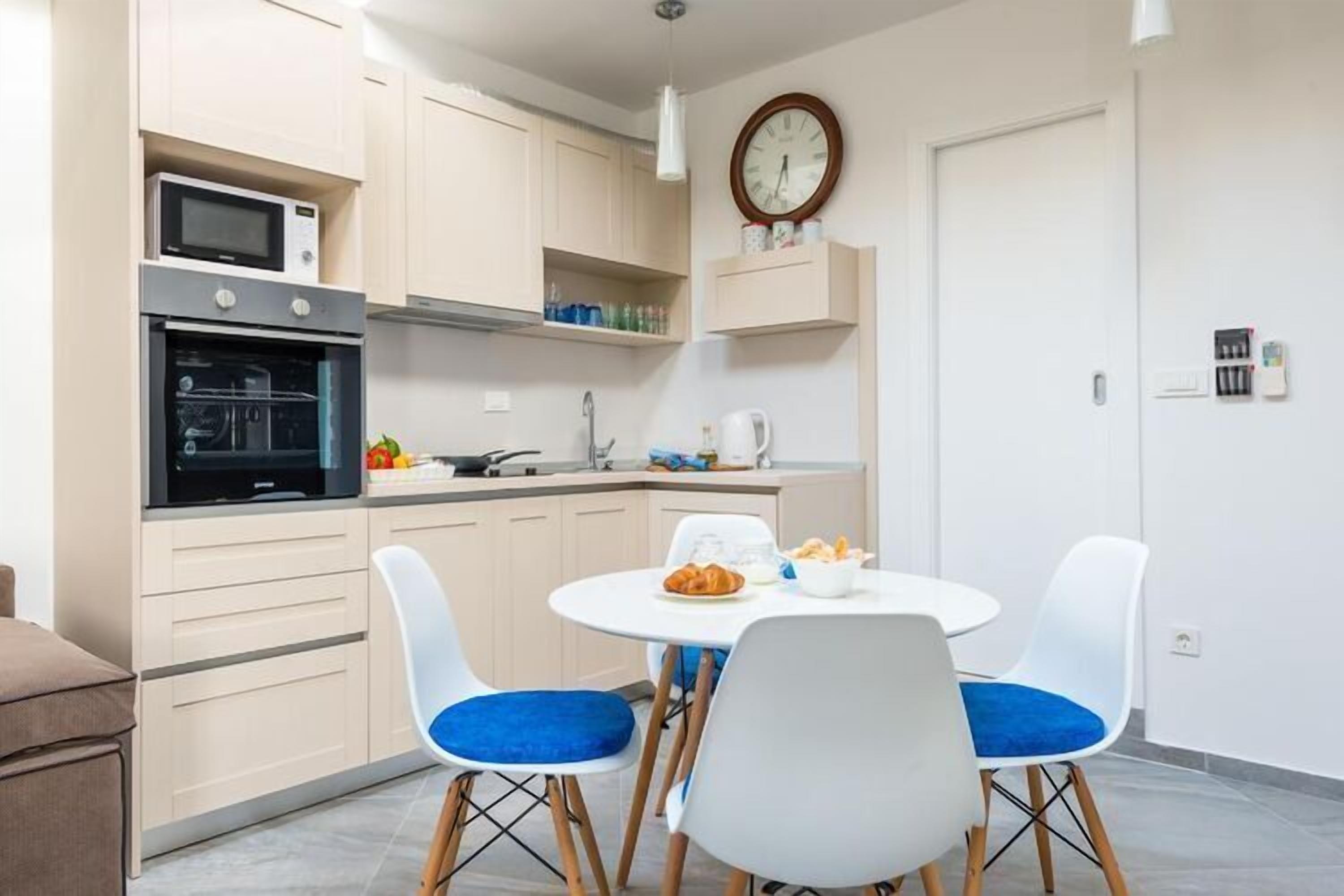 Une cuisine compacte dotée d’appareils électroménagers modernes, un coin repas avec deux chaises et une horloge au mur.