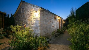 A stone building with a sloped roof, surrounded by potted plants and a gravel path. - Stone House Harmony - One Bedroom Apartment with Patio and Garden View ( 1 ) (Zrnovo)