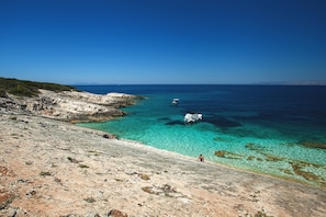 A coastal landscape with clear turquoise waters, rocky terrain, and a distant boat.