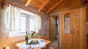 A wooden dining table with a lace tablecloth, a bottle of wine, and a vase with flowers. - Stone House Harmony -Studio Apartment with Patio and Garden View ( 2 ) (Zrnovo)