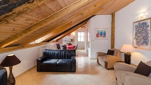 Un espacio habitable estilo loft con vigas de madera a la vista, un sofá de cuero negro, un sofá color beige y una zona de comedor con una mesa roja.